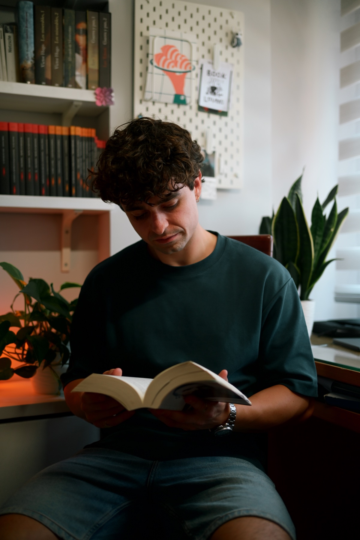 Néstor Baruque leyendo un libro junto a su biblioteca